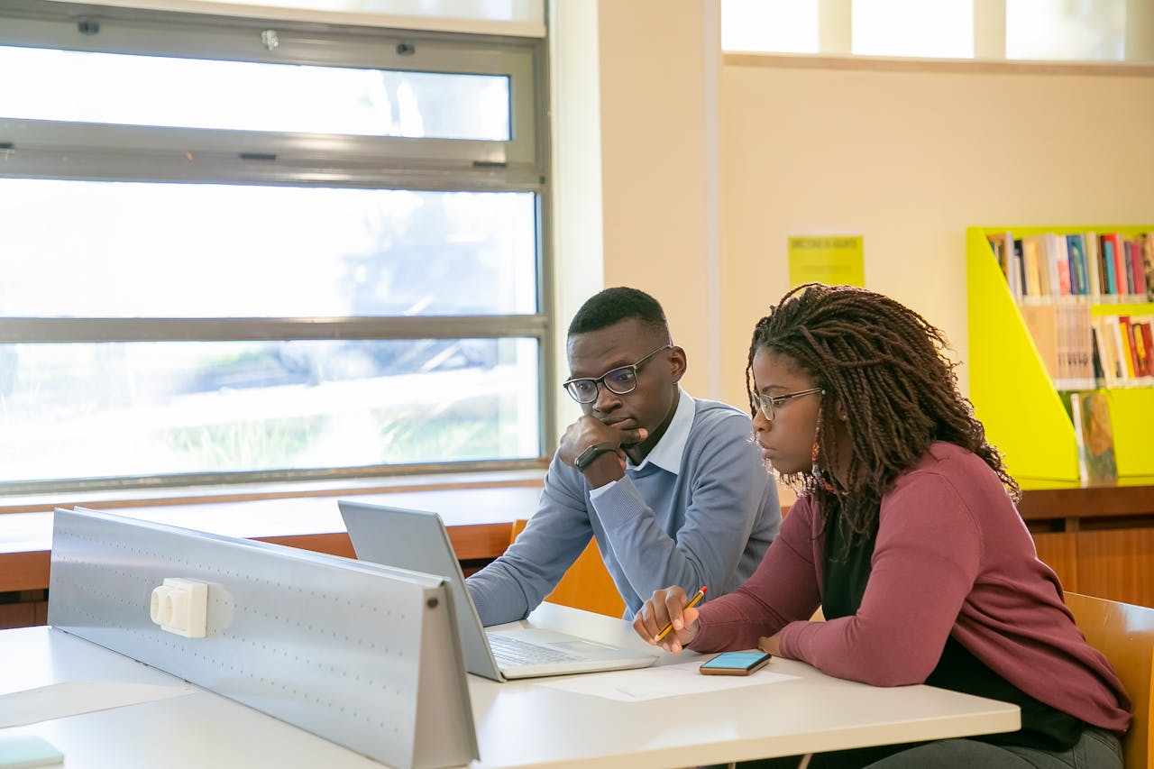 Young African American couple studying with a laptop in a library setting, emphasizing teamwork and focus.