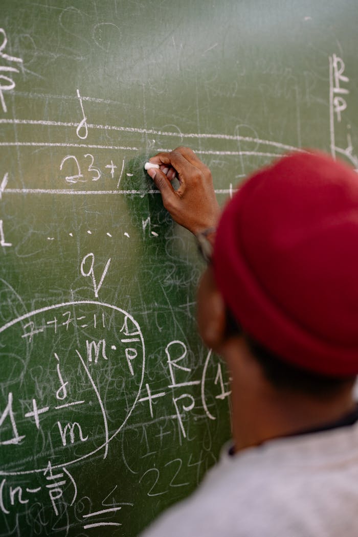 Person writing complex mathematical equations on a blackboard, focusing on education and learning.
